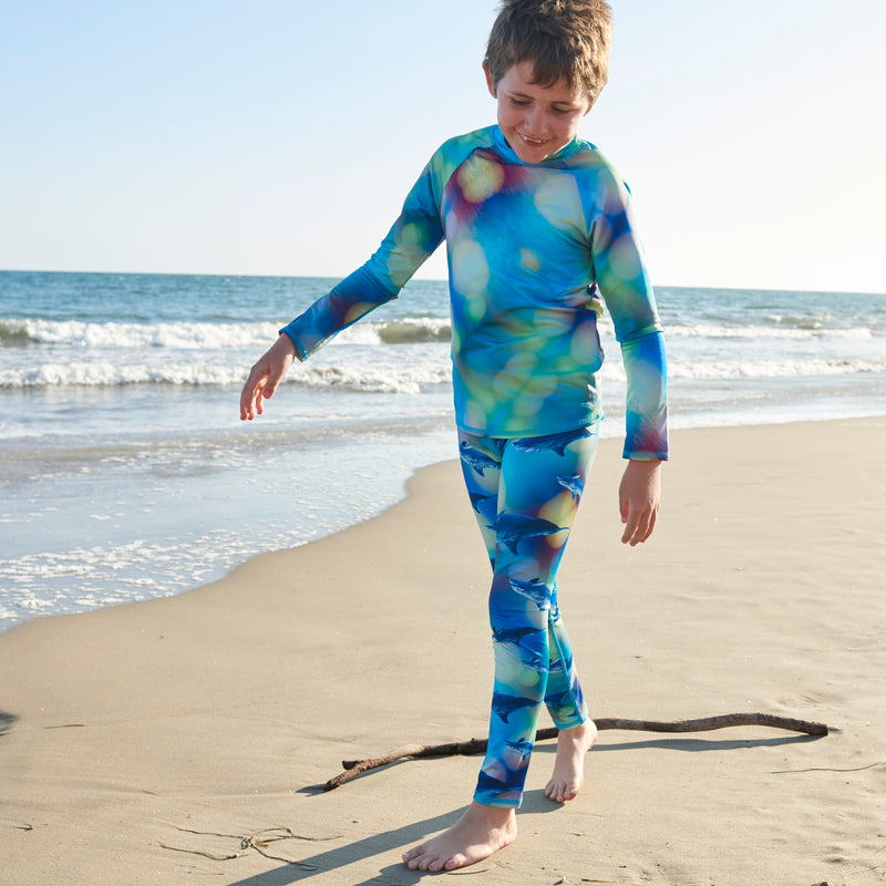 Child jogging on the shore wearing a printed rash guard from Sun Pop Life