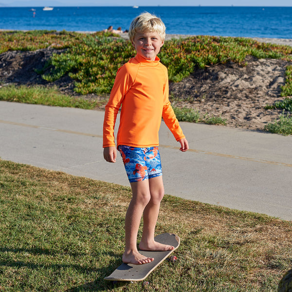 Bright Orange Kids Long Sleeve Rash Guard Top Upf50 Boys Girls Unisex Size 2 12 Boy Wearing a Bright Orange Top Standing on a Skateboard Sunpoplife