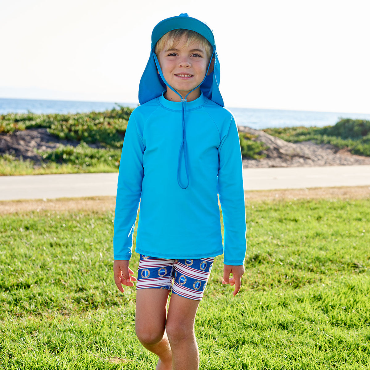 Island Blue Kids Long Sleeve Rash Guard Top Upf50 Boys Girls Unisex Size 2 12 Boy Walking on a Grassy Patch by the Beach Sunpoplife